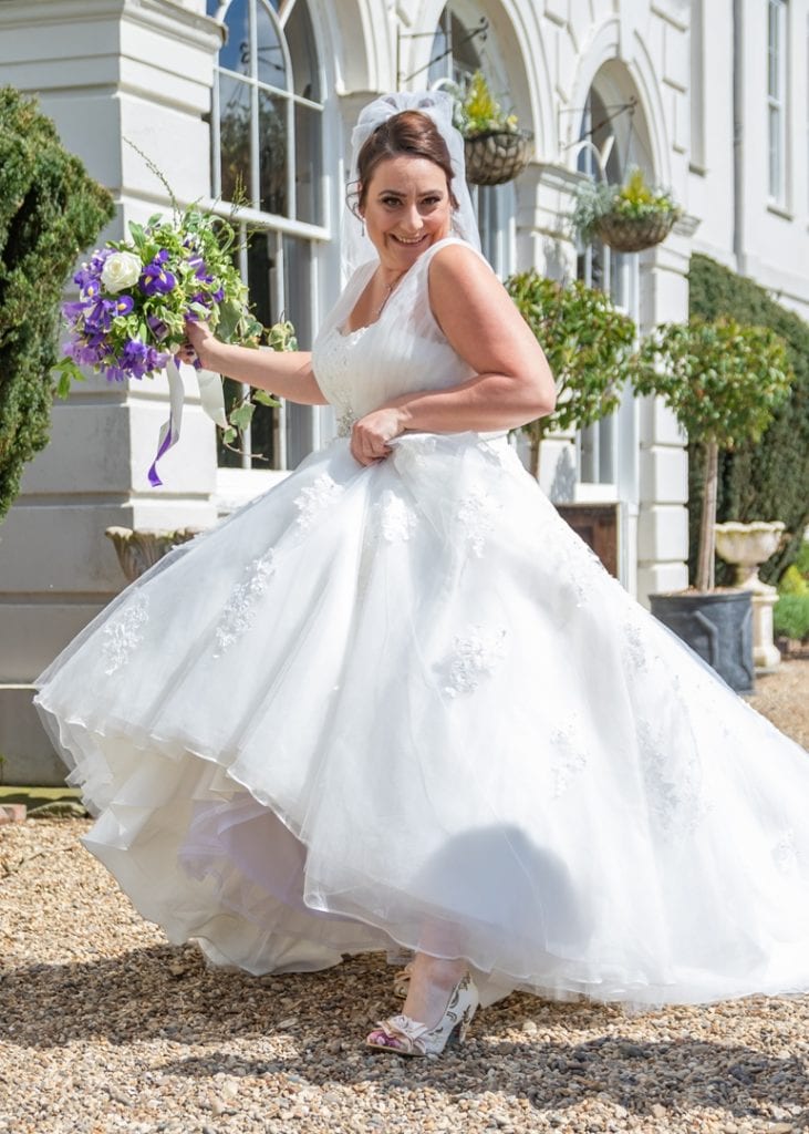 photo of bride holding her dress up smiling walking along with archways behind her