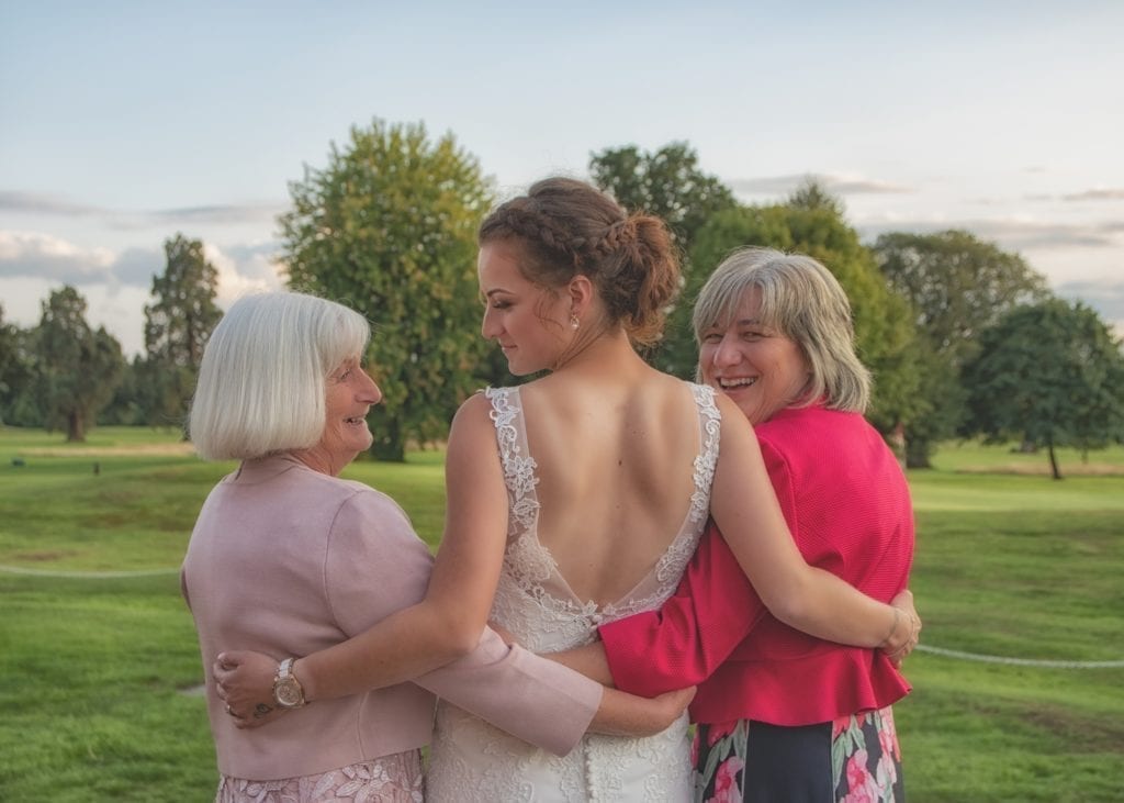 photo of bride embracing 2 women with fields and trees in the distance